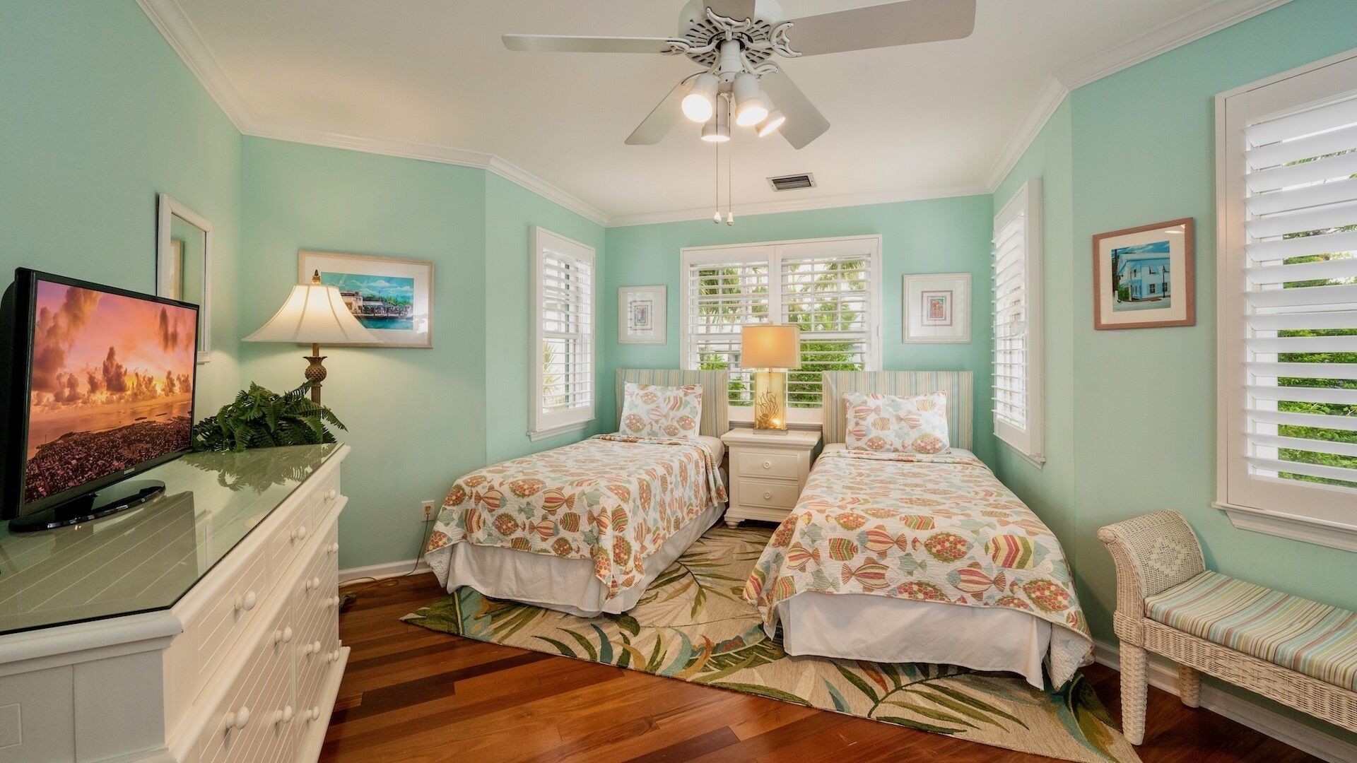 A bedroom with two beds, a TV, and a ceiling fan.