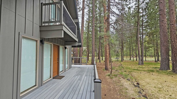 Ein modernes Gebäude mit einer Holzterrasse, großen Fenstern und einem Balkon mit Blick auf ein bewaldetes Gebiet.