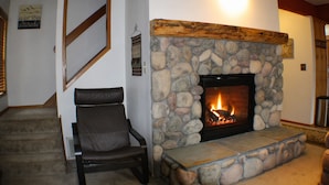 Ein Kamin aus Stein mit Feuer, ein Ledersessel und eine Treppe.