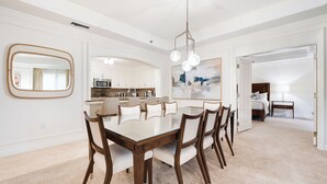 Un'area pranzo moderna con un tavolo in vetro, sedie di legno, un grande specchio e un lampadario contemporaneo.