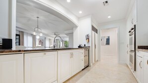 Una cucina moderna con mobili bianchi, un piano di lavoro in granito e una ventola a soffitto.
