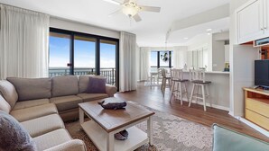 A modern living room with a sofa, coffee table, and a dining area with chairs and a table. - Leave your worries behind in this Relaxing Gulf Condo! - Recently Updated! (Orange Beach)