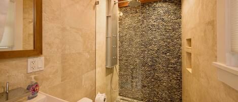 A bathroom with a stone wall, a shower, and a sink.