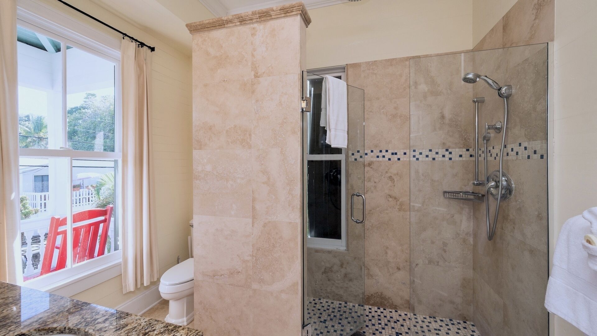 A modern bathroom with a glass-enclosed shower, a toilet, and a large window with a view of a balcony.