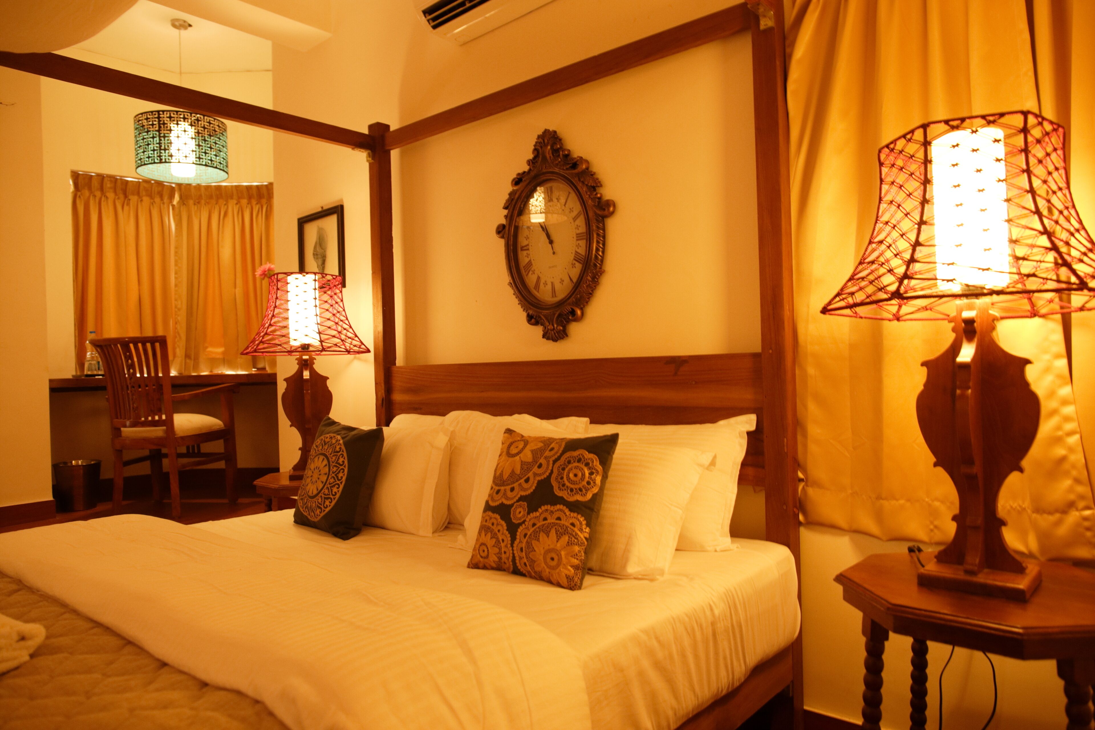 A hotel room with a large bed, two bedside lamps, a wooden headboard, a wooden nightstand, a chair, a desk, and a mirror on the wall.