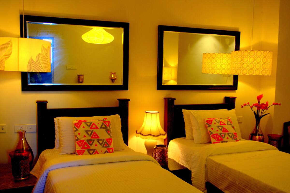 Ein Hotelzimmer mit zwei Betten, einem Nachttisch mit Lampe, einer Vase mit Blumen und einem Spiegel an der Wand.