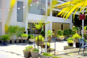 A courtyard with potted plants, a blue chair, and a building with large windows and a balcony. - Hotel Villa Highnest - Sriperumbudur (Sriperumbudur)