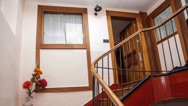 A staircase with wooden steps and a metal handrail, leading to a room with a window and a vase of flowers. - Authentic attic in the center of Béjar (Béjar)