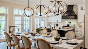 Een moderne keuken met een groot eiland, hanglampen en een eethoek met een tafel voor vier personen.