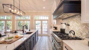 Een moderne keuken met een groot eiland, een gasfornuis en een backsplash met een visgraatpatroon.
