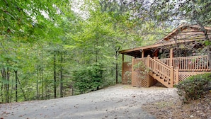 A cabin with a wooden deck and a covered porch, surrounded by dense forest.