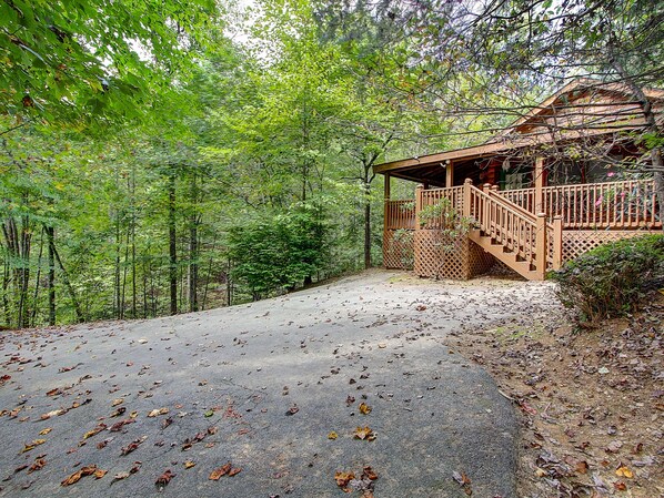 Une cabane dotée d’une terrasse en bois et d’un porche abrité, entourée d’une forêt dense.