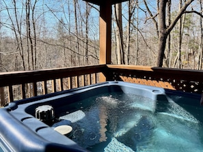 Un bain à remous sur une terrasse en bois, avec en arrière-plan des arbres sans feuilles.