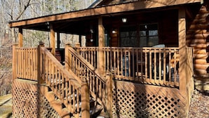 A wooden cabin with a covered porch and a staircase leading to a deck.