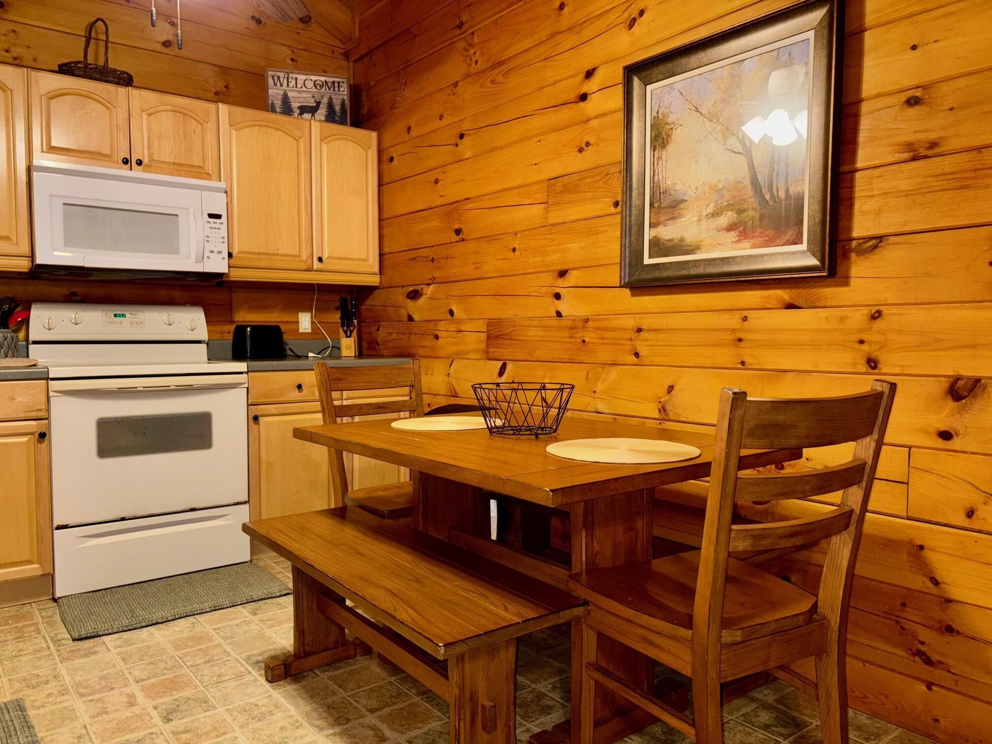 A wooden cabin interior with a kitchen area, including a stove, microwave, and wooden cabinets.
