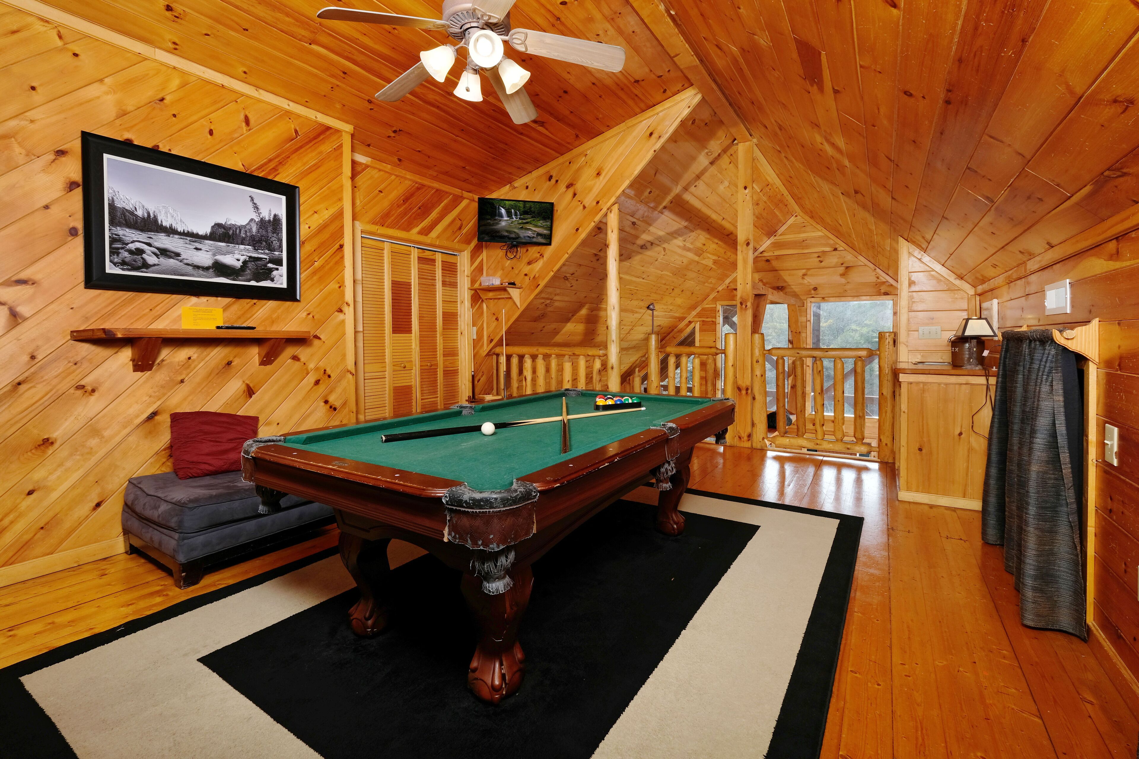 A wooden interior with a pool table, a ceiling fan, and a framed photograph on the wall.