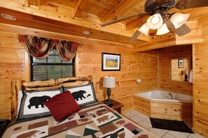 Habitación tipo cabaña de madera con una cama, una ventana con cortinas, un ventilador de techo, un cuadro enmarcado y un baño con bañera.