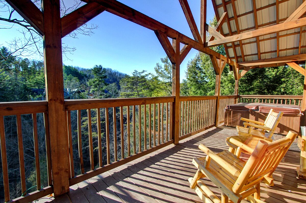 Une terrasse en bois avec une rambarde, des chaises en bois et une table, donnant sur une zone boisée.