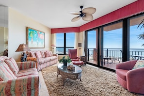 A spacious living room with a large window offering a view of the ocean, a ceiling fan, and a red accent wall.