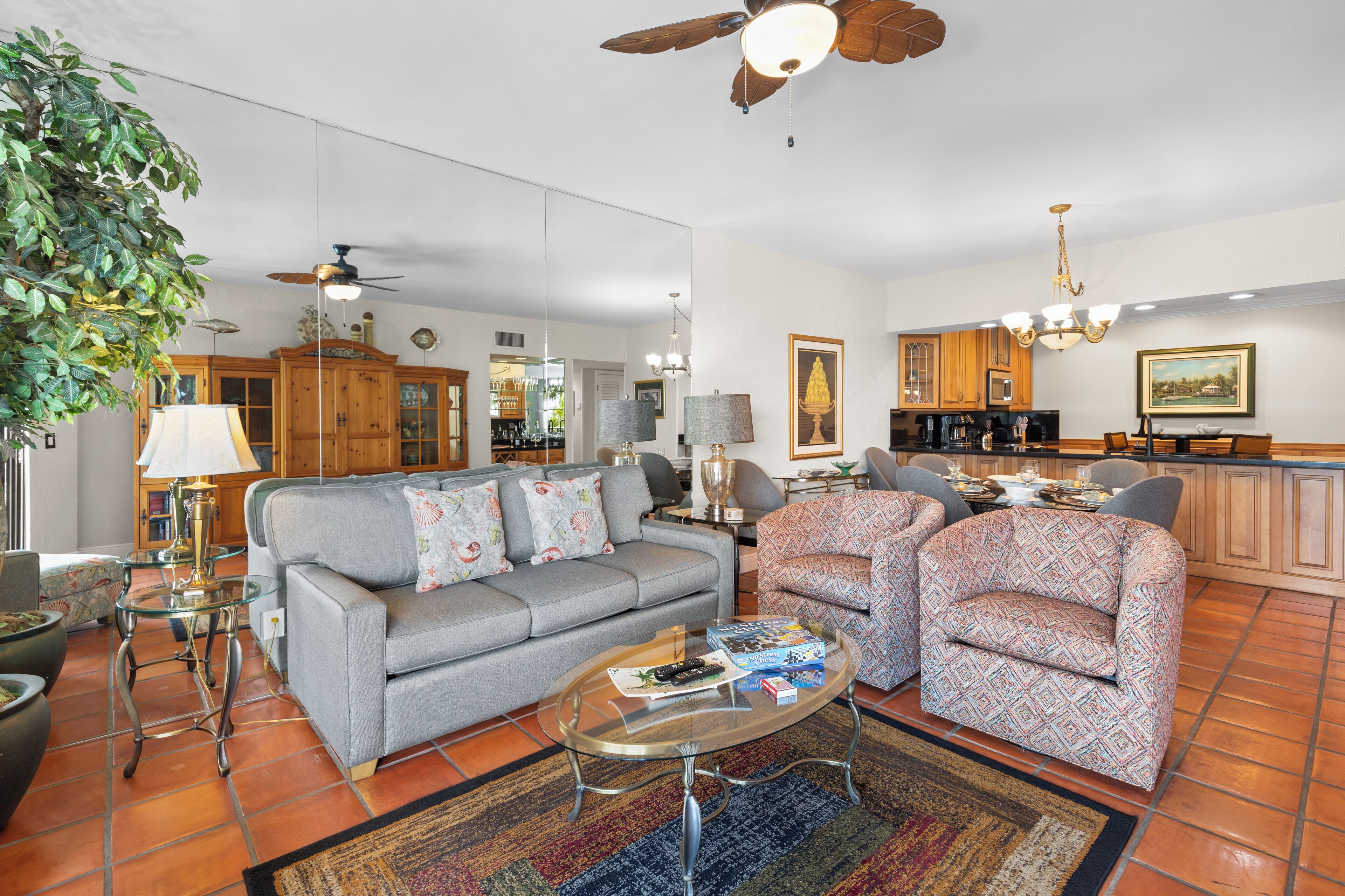 A spacious living room with a grey sofa, patterned armchairs, a coffee table, and a ceiling fan.