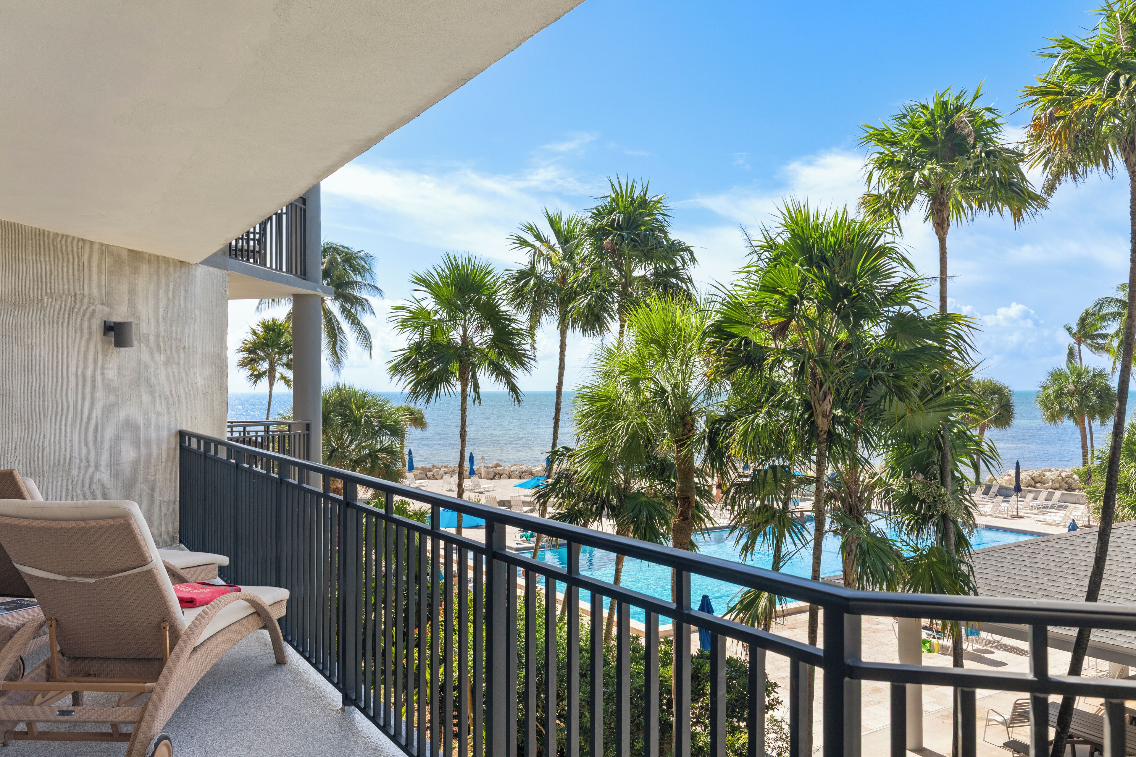 A balcony with a view of a pool and palm trees, overlooking a beach.