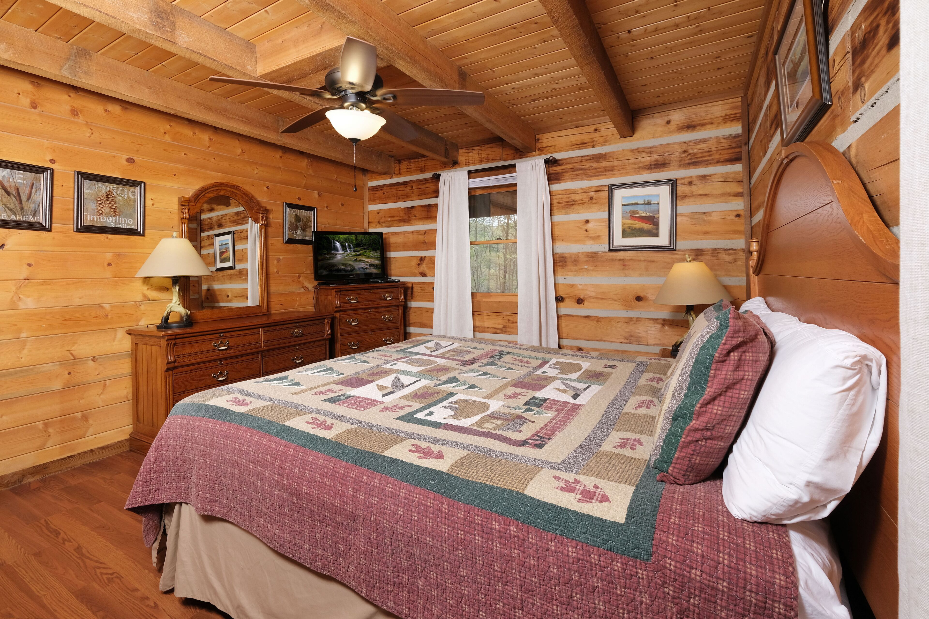 Ein Schlafzimmer einer Holzhütte mit Bett, Schminktisch und Deckenventilator.