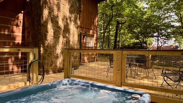 Una vasca idromassaggio in un’area con decking in legno, una parete in pietra e recinzione in metallo.