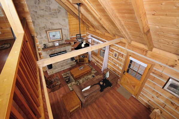 L’intérieur chaleureux d’un chalet avec un mur en pierre, des poutres en bois, un canapé agrémenté d’un ours en peluche et une cheminée.