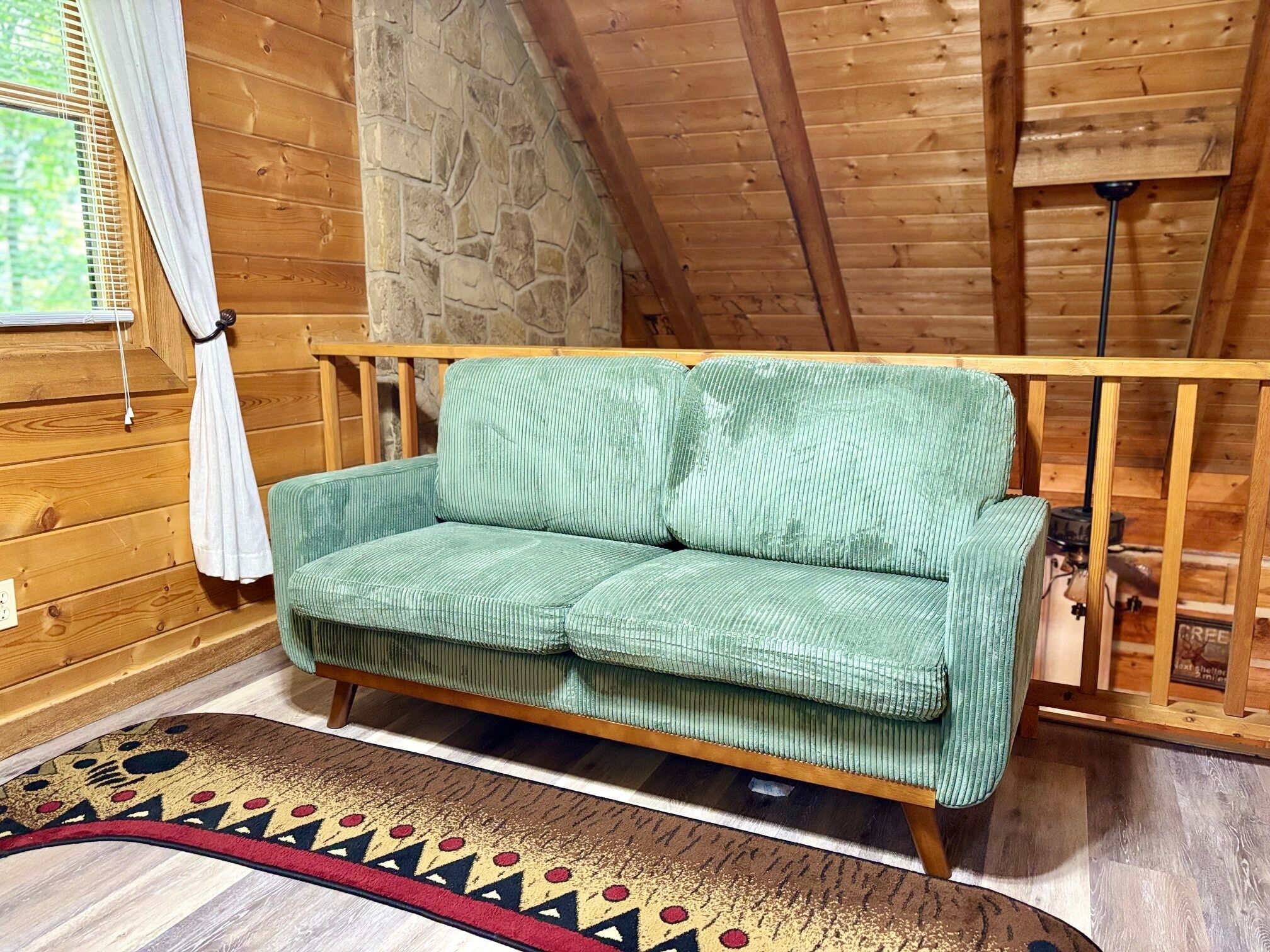 A cozy room with a green sofa, wooden walls, a stone accent wall, and a patterned rug.