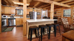 Una cucina in stile rustico con mobili in legno, un'isola centrale con sgabelli e un'area pranzo con tavolo e sedie in legno.
