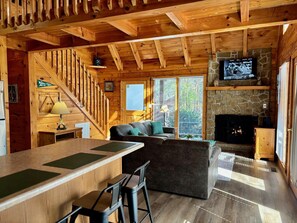 A wooden cabin interior with a staircase, a fireplace, a television, and a bar area.