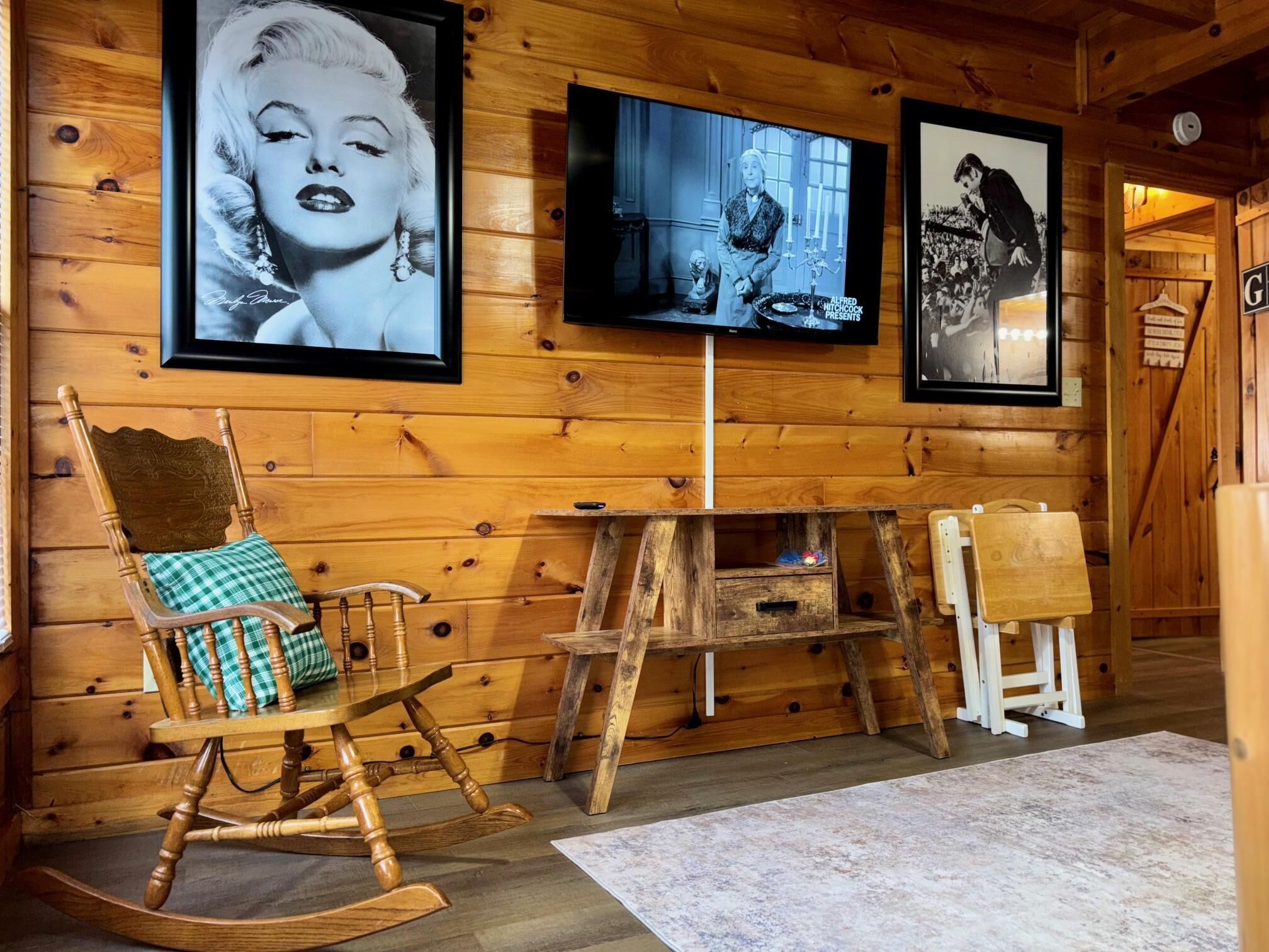 A wooden interior with a rocking chair, a television mounted on the wall, and framed pictures.