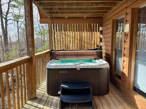 A wooden deck with a hot tub, a bench, and a window with blinds. - Pet friendly, hot tub, cozy log cabin sleeps 7! (Sevierville)