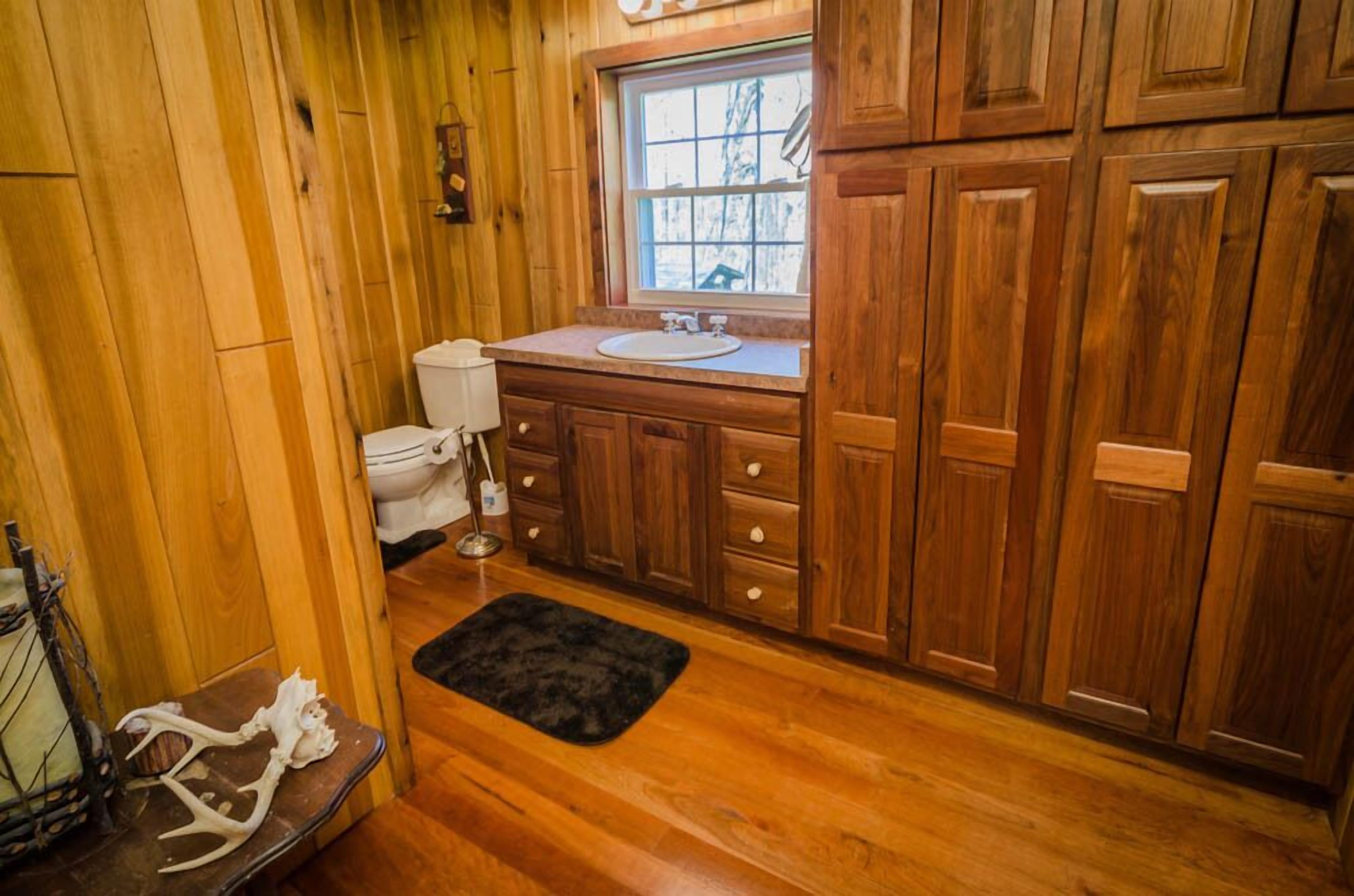 A wooden cabin bathroom with a wooden vanity, a toilet, and a window.