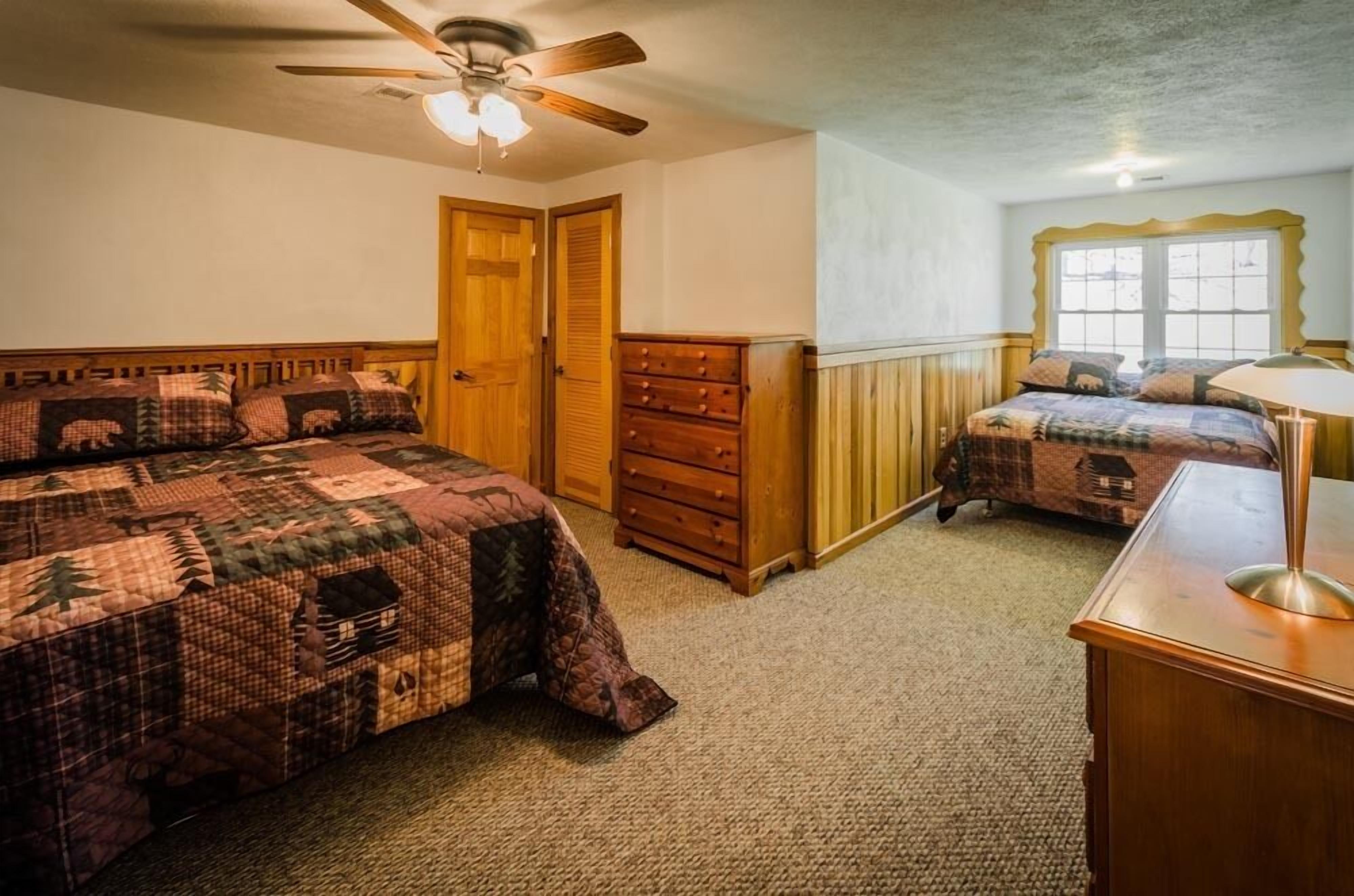 A bedroom with two beds, wooden furniture, a ceiling fan, and a window.