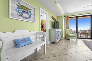 Relax in a spacious living area with a flat-screen TV, green armchair, and sliding glass door leading to a balcony with a clear view.