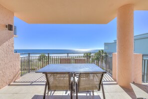 A balcony with a table and chairs, overlooking a beach.