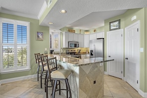 Modern kitchen with a central island, stainless steel appliances, and a window with blinds.