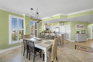A dining area with a white table and chairs, a chandelier, and a view of the outdoors through large windows.