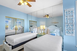 Two single beds with matching headboards and bedside tables, a large mirror, and a ceiling fan create a serene atmosphere.