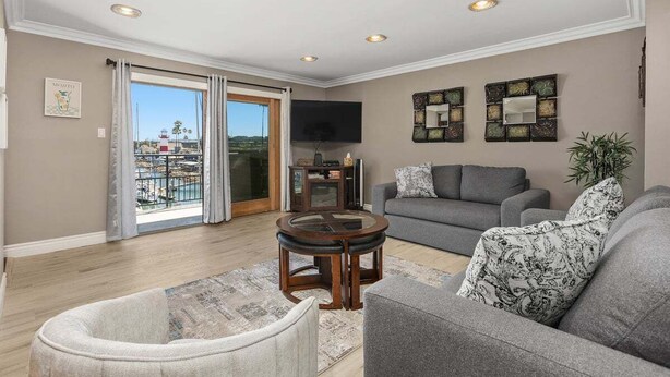 A living room with a grey sofa, a round coffee table, a grey armchair, a TV mounted on the wall, and a balcony with a view. - Beachfront Condo with Heated Pool and Hot Tub | 311B (Oceanside)