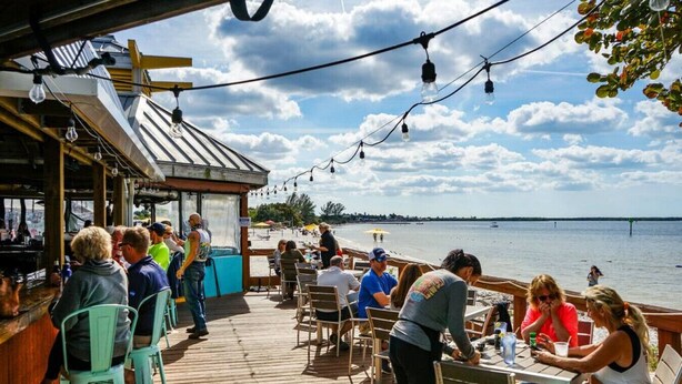A wooden deck with outdoor seating overlooking a body of water, a bar area, and a covered section with a view of the beach. - 3250 - Peace at Sea-Little Harbor Beach Resort - Tampa Bay (Ruskin)