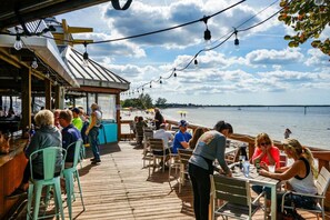 Een houten terras met buitenmeubilair, uitzicht op een waterpartij, een bar en een overdeeld gedeelte met uitzicht op het strand.