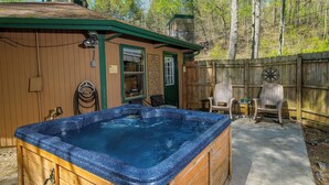 A wooden hot tub with a stone chimney, surrounded by a wooden fence and chairs.