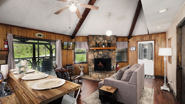 A cozy cabin interior with a stone fireplace, wooden dining table, and a comfortable seating area.