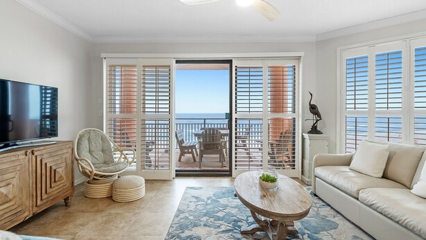 A living room with a television, a wicker chair, a sofa, a ceiling fan, and a view of the ocean through a sliding door. - 604W - Beachfront condo with Amazing views! (Orange Beach)