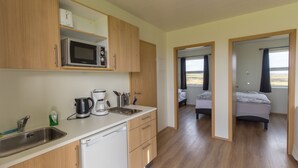 A compact kitchen with a microwave, coffee maker, and sink. There is a bed visible through an open door in the adjacent room.