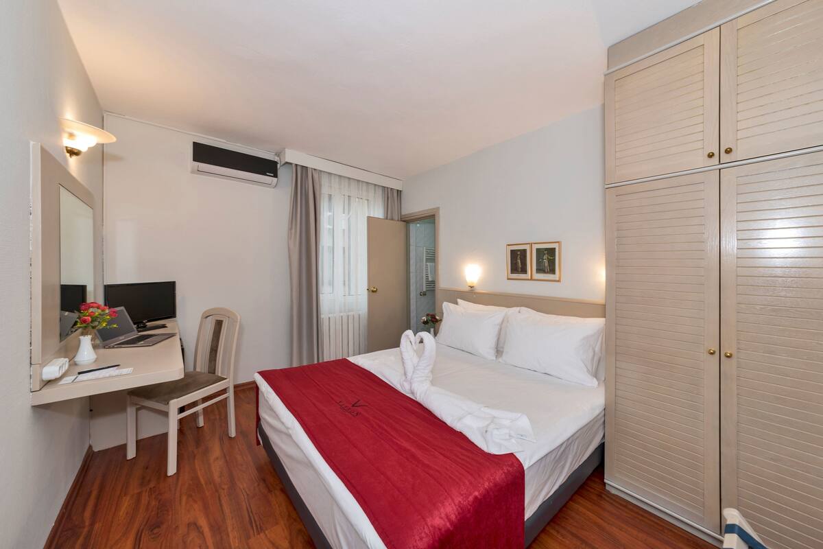 Habitación de hotel con cama, escritorio con computadora, silla, armario y espejo.