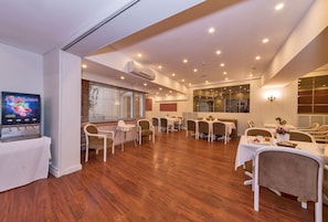 Un grand espace dédié à la salle à manger, avec plusieurs tables et chaises, un appareil de climatisation et un téléviseur placé sur le côté gauche.