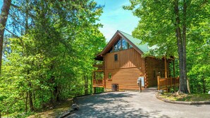 A log cabin with a porch, surrounded by dense forest. - Great location with hot tub and pool table! Cute and classy log cabin! (Sevierville)